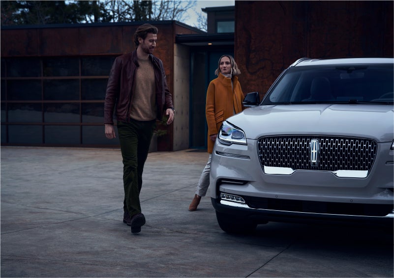 A man and a woman approaching a 2023 Lincoln Aviator® SUV, which illuminates certain lights when they are close | Pilson Lincoln in Mattoon IL