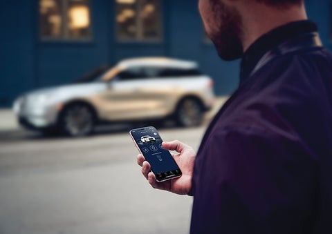 A person is shown interacting with a smartphone to connect to a Lincoln vehicle across the street. | Pilson Lincoln in Mattoon IL